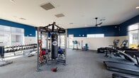 Located at 5151 N 95th Ave in Glendale, Arizona, this single-floor fitness center is a comprehensive workout facility designed to support a wide range of exercise routines. The space is defined by a bold two-tone color scheme — deep navy blue accent walls paired with crisp white — giving the interior a modern, energetic aesthetic. Durable carpet tile flooring covers the main workout area, while a dedicated studio room features warm hardwood flooring.

The main fitness floor is generously sized and bathed in natural light from large floor-to-ceiling windows and clerestory windows along the upper walls, offering views of the surrounding outdoor amenity areas, including a pool. Ceiling fans throughout aid in air circulation. Equipment includes a Life Fitness multi-station cable machine with a TKO heavy bag, a full dumbbell rack, adjustable benches, a stair climber, cable pulleys, and a row of Life Fitness treadmills and ellipticals. A water fountain station and direct exterior access add convenience.

A separate studio room is outfitted with spin bikes, TRX suspension trainers, medicine balls, and wall-to-wall mirrors, making it ideal for group or individual training sessions. The thoughtful layout, abundant natural light, and diverse equipment selection make this facility a standout amenity.