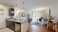 Located at 1 Gradient Court in Weymouth, MA, this 1-bedroom, 1-bathroom residence offers a thoughtfully designed open-concept layout. The combined kitchen and living area serves as the heart of the home, featuring warm hardwood-style flooring and an abundance of natural light streaming through large sliding glass doors that lead to an outdoor area. The kitchen is equipped with stainless steel appliances, including a refrigerator, microwave, and range, complemented by rich dark cabinetry and a granite-topped island with pendant lighting — ideal for both cooking and casual dining. The living area provides a comfortable and airy atmosphere with clean white walls and generous proportions. The bedroom offers a serene retreat with plush carpeting, a window with views, and a walk-in closet outfitted with wire shelving for organized storage. The bathroom includes a full tub-shower combination with white tile surround and built-in open shelving for added convenience. Clean lines and neutral tones throughout give the space a modern, cohesive aesthetic. The efficient single-floor layout maximizes every square foot, making this residence a practical and stylish option in the Weymouth community.