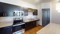 Located at 17571–17587 Dodd Blvd in Lakeville, Minnesota, this single-floor residence offers a well-designed, open-concept layout that seamlessly connects the kitchen and living areas. The kitchen is a standout feature, equipped with stainless steel appliances including a refrigerator, electric range, microwave, and dishwasher. Rich, dark cabinetry pairs elegantly with granite countertops, and a decorative lattice wine rack adds a distinctive touch. Pendant lighting above the kitchen island enhances the functional yet stylish atmosphere. The open living area extends naturally from the kitchen, highlighted by durable hardwood-style flooring, a ceiling fan, and access to a private outdoor space through a glass door framed by windows that invite natural light. Bedrooms are carpeted for comfort, each featuring ceiling fans, and at least one bedroom benefits from an expansive walk-in closet outfitted with multi-level wire shelving systems for generous storage. The bathrooms are finished with granite-topped dark vanities, chrome fixtures, and full tub-shower combinations. Consistent use of granite countertops, dark cabinetry, and hardwood-style flooring throughout creates a cohesive, modern aesthetic across the entire space.