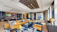 Located at 1650 NE 124th St in North Miami, FL, this sophisticated lounge offers a generously proportioned, single-floor open layout designed with modern luxury in mind. The space is anchored by a striking coffered ceiling adorned with an eye-catching cluster of globe pendant lights, creating a dramatic focal point that sets an upscale tone throughout.

The main living area features a bold, curated seating arrangement with a vibrant mustard-yellow leather sectional sofa, complementary blue ottomans, and a classic Eames lounge chair, all centered on a patterned area rug over elegant chevron-patterned hardwood flooring. Large-scale abstract artwork and sculptural accents add to the refined ambiance.

A dedicated bar and counter area runs along one side of the lounge, equipped with seating for multiple guests, large wall-mounted displays, and pendant lighting overhead — ideal for social gatherings. A shuffleboard table nearby offers an entertaining recreational element.

Floor-to-ceiling windows and glass doors along the perimeter bathe the entire lounge in abundant natural light while providing views of the surrounding outdoor area. The entryway corridor features clean architectural lines with slatted ceiling details, warm wood-paneled walls, and blue accent chairs, creating a welcoming transition into the main lounge area.
