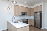 Located at 13450 W Baldcypress St in Boise, Idaho, this 2-bedroom, 2-bathroom residence offers a thoughtfully designed single-level layout with contemporary finishes throughout. The open-concept kitchen serves as the heart of the home, featuring light wood cabinetry, white quartz countertops, a subway tile backsplash, and a full suite of stainless steel appliances including a refrigerator, electric range, built-in microwave, and dishwasher. Pendant lighting above the kitchen peninsula adds a modern touch, while wood-look flooring flows seamlessly into the adjacent living area. The living space is bright and welcoming, with access to a private balcony through glass-paned doors that frame views of the surrounding landscape. Both bedrooms are generously proportioned, featuring plush carpet, natural light from horizontal-blind windows, and ample closet space. The two full bathrooms are finished with wood-toned vanity cabinetry, white quartz surfaces, wood-look tile flooring, and full tub-shower combinations with white subway tile surrounds. Clean lines, neutral tones, and consistent modern detailing create a cohesive and comfortable living environment throughout the entire unit.