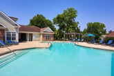 Located at 900 Meadow Glen Pkwy in Fairburn, Georgia, this outdoor pool area serves as a standout community amenity designed for relaxation and recreation. The generously sized swimming pool features a gently curved shape with clearly marked depth zones, accommodating both casual swimmers and those seeking a refreshing dip. Finished with tile detailing along the waterline and bordered by a wide concrete sundeck, the pool area provides ample space for lounging and socializing.

The sundeck is well-equipped with numerous lounge chairs arranged around the perimeter, offering residents plenty of seating options to enjoy the open-air setting. Colorful umbrellas and a pergola structure provide shaded retreats, adding both function and visual interest to the space. The pool is enclosed by a wrought iron fence, ensuring safety while maintaining clear sightlines to the surrounding mature trees and landscaping that lend a sense of privacy and tranquility.

Adjacent to the pool is a single-story clubhouse structure featuring a combination of brick and siding exterior, large windows, and a covered entryway — providing a convenient indoor facility directly accessible from the pool deck. The overall atmosphere is bright and inviting, benefiting from abundant natural light and a well-maintained landscape that enhances the resort-like character of this community amenity.