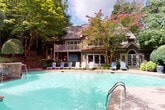 This inviting outdoor amenity space is thoughtfully designed to offer a resort-like experience surrounded by nature. At its centerpiece is a generously sized swimming pool with crystal-clear turquoise water, framed by a row of white lounge chairs perfect for relaxing in the sun. The main building features a charming upper-level deck with wooden railings, complemented by blooming crepe myrtles and mature trees that provide natural shade and vibrant color throughout the seasons.

Extending from the pool area is a spacious wooden deck that serves as a central gathering space. Furnished with additional lounge chairs and outdoor seating, it connects seamlessly to a pergola-covered section fitted with built-in bench seating and pendant lanterns, creating a shaded retreat nestled beneath the tree canopy. The open-beam pergola design allows filtered natural light to flow through while offering a sense of shelter and intimacy.

A separate wooden deck area features a handsome gazebo with a stone base, cedar framing, and a shingled roof, adding an architectural focal point to the landscape. Manicured greenery and natural wooded surroundings border the entire space, enhancing the sense of seclusion and tranquility. Collectively, these outdoor areas provide a well-appointed environment ideal for leisure, socializing, and relaxation.