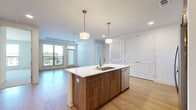 Located at 1003 Ridgewalk Pkwy in Woodstock, GA, this well-appointed 2-bedroom, 3-bathroom residence offers a thoughtfully designed single-floor layout. The open-concept kitchen and living area serves as the heart of the home, anchored by a striking center island with a waterfall-edge quartz countertop, an undermount sink, and warm walnut-toned cabinetry accented by gold hardware. Pendant lighting illuminates the island, while stainless steel appliances, a hexagonal tile backsplash, and upper white cabinetry complete the kitchen. The living area benefits from large windows and sliding glass door access to a balcony, offering pleasant outdoor views and filling the space with natural light. Light wood-tone flooring runs throughout the main living areas, creating a clean, contemporary aesthetic. The bedrooms feature plush carpeting, and the spacious primary bedroom includes a walk-in closet with built-in wire shelving. A second generous closet provides additional storage. The bathrooms are finished with white quartz vanities, wood-framed mirrors, and glass-enclosed walk-in showers. The overall ambiance is bright, modern, and move-in ready, with consistent finishes that lend a cohesive, polished feel throughout the entire residence.