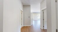Located at 52 Main St in Camillus, NY, this two-bedroom, one-bathroom unit offers a modern, loft-inspired aesthetic spread across a generously sized single floor. The open-concept kitchen and living area serves as the heart of the home, featuring warm hardwood-style flooring throughout, soaring ceilings with exposed industrial ductwork, and abundant recessed lighting. The kitchen is well-appointed with white shaker cabinetry, dark granite countertops, a center island with pendant lighting, a subway tile backsplash, and a full suite of stainless steel appliances. Tall, multi-pane windows flood the living area with natural light and offer pleasant views of the surrounding Camillus streetscape and greenery. The primary bedroom provides a comfortable footprint, complemented by natural light from large windows with neighborhood views. The second bedroom also features hardwood-style flooring, exposed ductwork, and a window with outdoor views. The bathroom is clean and contemporary, finished with large-format tile flooring, a sliding glass-enclosed shower with tile surround, a vanity with storage, and modern fixtures. Three closets throughout the unit provide ample storage. A hallway connects the rooms with clean white walls and high ceilings, reinforcing the open, airy character of this thoughtfully designed space.