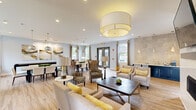 Located at 279 Lindenwood Dr in Exton, PA, this single-floor community space offers a thoughtfully designed open-concept layout that seamlessly integrates a dining room and living room into one cohesive environment. Light hardwood-style flooring flows throughout, complementing the soft blue-gray walls and crisp white trim for a clean, contemporary aesthetic.

The dining area features multiple seating arrangements, including a round dark wood table with cross-back chairs and a larger rectangular white table with modern upholstered seating, all illuminated by elegant globe pendant lights and track lighting. Curated abstract artwork adorns the walls, adding a sophisticated touch. A shuffleboard table provides a recreational focal point.

The living area is anchored by a sleek wall-mounted fireplace and a flat-screen TV, flanked by comfortable neutral sofas and accent chairs dressed with yellow throw pillows. A striking textured tile accent wall frames a built-in wet bar with navy cabinetry and a white countertop, illuminated by teardrop pendant lights.

Large double-hung windows dressed with gray and yellow two-tone curtains flood the space with natural light and offer outdoor views of the surrounding greenery. French doors provide convenient access to the exterior, enhancing the bright and welcoming ambiance throughout.