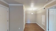 This single-floor, one-bedroom, one-bathroom unit offers a thoughtfully designed layout that maximizes functionality and comfort. Throughout the main living areas, rich dark hardwood-style flooring contrasts beautifully with the neutral warm-gray walls and crisp white trim, creating a clean and cohesive aesthetic. Crown molding adds a refined architectural detail throughout, lending the space an elevated feel.

The open living area is anchored by a ceiling fan with a light fixture, providing both comfort and illumination, and benefits from a window that allows natural light to filter in. A pendant light fixture highlights the dining area, which flows seamlessly into the rest of the space. A tall, paneled storage cabinet near the entry adds practical storage without compromising the open feel of the floor plan.

The kitchen is well-equipped, featuring white cabinetry, a classic subway tile backsplash, granite-style countertops, and black appliances including a refrigerator and an electric range with an overhead ventilation hood.

The bedroom is generously proportioned, featuring the same dark hardwood-style flooring, a ceiling fan, crown molding, and a window with blinds that invites natural light. The bathroom includes a full tub-shower combination with clean white tile surround and polished chrome fixtures, offering a simple and functional design.