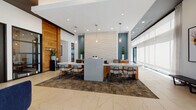 This contemporary amenity floor showcases a thoughtfully designed interior that blends professional functionality with inviting social spaces. The main leasing area serves as a striking centerpiece, featuring a large central island with quartz countertops, warm wood accents, and a textured stone tile feature wall framed by teal accent panels. Sleek pendant lighting hangs above workstations, while expansive windows flood the space with natural light, complemented by polished marble-look tile flooring throughout.

The social lounge offers a sophisticated bar area with a bold geometric-patterned tile backsplash, a wall-mounted TV, warm wood paneling, and a generous quartz-topped bar counter with modern upholstered seating. Adjacent to the bar, a bistro-style high-top table with bar stools sits beside a curated gallery wall of nature-inspired artwork.

A dedicated co-working lounge features built-in desk stations within warm amber-toned alcoves, pendant lighting, and mixed seating including velvet armchairs and task chairs, ideal for focused work or casual collaboration. A quieter seating nook provides plush blue armchairs set against a richly textured feature wall, offering a more intimate retreat.

Wide, well-lit corridors with marble-look tile and tasteful greenery connect each zone, creating a seamless and polished flow throughout the entire floor.