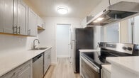 Located at 1831 13th Ave E in Bradenton, Florida, this single-floor unit offers a clean, modern aesthetic throughout. The open-concept living area is bright and airy, featuring light wood-style flooring, crisp white walls, and a ceiling fan. A large picture window allows natural light to pour into the space, creating a welcoming atmosphere. The living area flows seamlessly from the kitchen, which is separated by a half-wall partition.

The galley-style kitchen is well-appointed with gray shaker-style cabinetry, light quartz countertops, and a full suite of stainless steel appliances including a refrigerator, electric range, dishwasher, and range hood. The light wood flooring continues throughout, lending a cohesive feel to the space. A door from the kitchen provides additional access, adding to the unit's functional layout.

The bathroom features elegant marble-look tile covering both the floor and the tub surround, complemented by a standard white vanity and brushed nickel fixtures. The overall design of the space is fresh and updated, with a neutral color palette that enhances its bright, open character. The layout is practical and efficient, making excellent use of the available footprint on a single level.