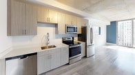 Located in the heart of Miami's vibrant Brickell district, this single-floor unit offers a contemporary urban living experience defined by clean lines and modern finishes throughout. The open-concept layout is anchored by a well-appointed kitchen featuring light wood-grain cabinetry extending from floor to ceiling, a white quartz countertop, a stainless steel undermount sink with an industrial-style faucet, and a full suite of stainless steel appliances including a French door refrigerator, electric range, and built-in microwave. An exposed concrete ceiling adds an industrial-chic aesthetic that carries throughout the living space, complemented by light wood-look flooring that unifies the entire unit. The living area is a standout, bathed in abundant natural light through expansive floor-to-ceiling sliding glass doors that frame breathtaking panoramic views of the Miami skyline. A bold navy accent wall adds a pop of color against the otherwise crisp white interior. The bathroom is thoughtfully designed with wood-look tile flooring, large-format warm-toned wall tiles surrounding a soaking tub and shower combination, a white quartz vanity top, and an integrated undermount sink. This residence delivers a refined, modern aesthetic in one of Miami's most sought-after urban locations.