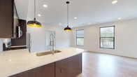 Located at 1050 N. 4th St in Columbus, Ohio's vibrant Short North area, this modern single-floor unit offers a thoughtfully designed open-concept layout with clean, contemporary finishes throughout. Light hardwood flooring flows seamlessly across the living, dining, and kitchen areas, creating a cohesive and inviting atmosphere.

The kitchen is a standout feature, showcasing dark cabinetry, a white quartz waterfall island with an undermount sink and high-arc faucet, stainless steel appliances including a range, microwave, and refrigerator, and a classic white subway tile backsplash. Stylish black pendant lights with gold interiors hang above the island, adding a modern touch.

The open living area benefits from multiple black-framed windows that draw in abundant natural light and offer views of the surrounding neighborhood. The bedrooms continue the light hardwood flooring and feature large windows with neighborhood views, providing a bright and airy feel.

Two well-appointed bathrooms include large-format white tile flooring and dark-framed vanities with white countertops. One bathroom features a tiled walk-in shower with sliding glass doors, while the other includes a tiled tub-shower combo with a glass enclosure. Recessed lighting throughout the unit ensures consistent, modern illumination across all spaces.