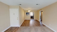 This single-floor, two-bedroom home offers a practical and comfortable layout designed for everyday living. The main living area greets you upon entry with warm hardwood-style flooring, neutral beige walls, and a ceiling fan with integrated lighting. A pass-through window connects the living space to the kitchen, enhancing the open feel of the common areas. The kitchen is well-appointed with dark espresso cabinetry, granite-style countertops, black appliances including an electric range, and a double-basin sink positioned beneath a window that brings in natural light. Both bedrooms are generously sized, featuring plush wall-to-wall carpeting and large windows that allow ample daylight. The primary bedroom includes access to a walk-in closet, providing notable storage capacity. The bathrooms are thoughtfully designed; one features a dark-cabineted vanity with a granite-style countertop and a three-light fixture above a large mirror, while another includes a tub-shower combination with tiled surround and wood-style flooring. Throughout the home, a consistent warm neutral palette, textured ceilings, and clean white trim create a cohesive and inviting atmosphere.