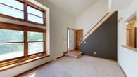 This two-story home offers a well-considered layout with distinct spaces across multiple levels. The main level immediately impresses with a grand entryway boasting dramatic vaulted ceilings that amplify the sense of openness. Large wood-trimmed windows flood the living area with natural light while framing views of lush, mature greenery outside. Soft carpeting transitions seamlessly to hardwood-style flooring at the entry, complemented by warm wood accents throughout. A striking dark accent wall borders the open staircase, which features a wood railing and leads to the upper level, adding a modern contrast to the otherwise light and airy palette of white walls and natural wood trim.

Accessible from the home is a covered outdoor porch that offers a serene retreat surrounded by mature flowering trees, providing a leafy, private setting ideal for relaxing outdoors.

The lower level houses a practical utility space that includes a full-size washer and dryer set alongside a water treatment system. The exposed concrete walls and open-joist ceiling with visible ductwork give this area a utilitarian character well-suited for storage and mechanical needs. Together, the levels of this home combine comfortable living spaces, outdoor access, and practical utility into a cohesive and functional residence.