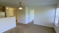 This single-floor residence offers a clean, functional layout designed for comfortable everyday living. The main living and dining area is finished with wall-to-wall carpeting in a warm neutral tone, creating a cohesive and inviting atmosphere throughout. Crisp white walls and white trim provide a bright, airy feel, while a classic pendant light fixture with a frosted glass shade anchors the dining area, adding a touch of understated elegance.

The open-concept design allows for a natural flow between the living space and the adjacent kitchen, which is partially visible and features a raised countertop bar — ideal for casual dining or meal prep. A doorway leads from the main area into a connecting room, suggesting a well-organized floor plan with clearly defined functional zones.

The space is characterized by its simplicity and practicality. Smooth ceilings with standard height contribute to the overall sense of openness, and the neutral color palette throughout makes the space highly adaptable to a variety of furnishing styles. The layout is straightforward and efficient, offering a comfortable single-level living experience with easy accessibility between all areas.