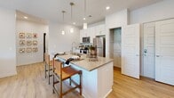 This single-floor residence offers a practical and stylish layout across two bedrooms and two bathrooms. The open-concept kitchen and living area form the heart of the home, featuring light hardwood flooring that flows seamlessly throughout. The kitchen is outfitted with white shaker cabinetry, a subway tile backsplash, stainless steel appliances, and a central island with a quartz countertop and pendant lighting overhead — ideal for both meal preparation and casual dining. The living room is bright and welcoming, with large sliding glass doors that open to a private balcony overlooking a scenic outdoor view, filling the space with abundant natural light. The primary bedroom is a comfortable retreat, complete with plush carpeting, a ceiling fan, a large window with outdoor views, and access to a dedicated bathroom featuring a white vanity with gold-tone fixtures and a walk-in closet with wire shelving. The second bedroom is equally well-proportioned, also carpeted, with clean neutral walls and its own closet. Both bathrooms are finished in a clean, contemporary palette. Two hallways connect the rooms efficiently, contributing to a logical and livable floor plan throughout this refined residence.