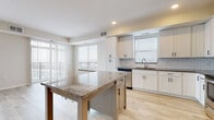 This single-floor residence is designed with a clean, contemporary aesthetic and a thoughtfully organized layout. The kitchen serves as a central highlight, featuring white shaker-style cabinetry with matte black hardware, granite countertops, a classic white subway tile backsplash, and a full suite of stainless steel appliances including a French door refrigerator, range, microwave, and dishwasher. A centrally positioned island with a granite surface offers built-in shelving and wine storage, providing additional prep space and casual seating. Light wood-style flooring runs throughout the main living areas, enhancing the bright, airy atmosphere.

The living area benefits from generous natural light, with large windows and a sliding glass door leading to an outdoor space. The bedrooms are carpeted and spacious, each equipped with a ceiling fan and ample natural light from well-placed windows. Panel-style doors add a modern touch throughout.

The bathrooms are finished consistently with white cabinetry, granite vanity tops, and light wood-style flooring. One bathroom includes a tub-shower combination with brushed nickel fixtures, while another features accessibility-oriented design elements including grab bars. Overall, the unit presents a cohesive, modern feel with neutral tones and quality finishes throughout.