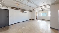 This single-floor studio unit delivers a distinctive industrial-loft character through its exposed ceiling infrastructure, including visible ductwork, conduit, and structural beams that lend an authentic urban aesthetic. Polished concrete floors run throughout the space, adding to the raw, modern sensibility.

The open main living area is bright and generously proportioned, featuring a wall-mounted mini-split HVAC unit, industrial-style cage light fixtures, and a window that invites natural light into the room. The layout provides a flexible, open canvas well-suited for a variety of configurations.

The kitchen is efficiently designed in a U-shaped layout, outfitted with sleek white flat-panel cabinetry, light-toned countertops, and a full suite of stainless steel appliances including a range, over-the-range microwave, dishwasher, and refrigerator. A pendant light fixture with Edison-style bulbs adds a warm, stylish accent overhead.

The bathroom is clean and functional, featuring a bathtub and shower combination with a grab bar, a standard toilet, and a ceiling-mounted industrial light fixture. The concrete flooring continues here, maintaining design consistency throughout.

A dedicated laundry area houses a stacked GE washer and dryer unit with external venting, offering the convenience of in-unit laundry. This space combines practicality with a bold, loft-inspired design identity.