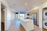 Located at 2950 Arkins Ct in Denver, CO, this modern one-bedroom, one-bathroom unit offers a thoughtfully designed open-concept layout with clean lines and contemporary finishes. The living and kitchen areas flow seamlessly together, anchored by a large white kitchen island with an integrated sink — ideal for both meal prep and casual dining. The kitchen is outfitted with light wood cabinetry, a white tile backsplash, quartz countertops, and a full suite of stainless steel appliances including a range, microwave, and refrigerator. Light wood-style flooring runs throughout the main living areas, lending warmth and continuity to the space. Large windows in the living area invite natural light and offer open views of the surrounding Denver cityscape. The bedroom is a well-proportioned retreat featuring plush carpet, a ceiling fan, and direct access to a dedicated walk-in closet with built-in shelving. The bathroom is finished in a crisp, minimalist style with a wood-toned vanity, white quartz countertop, and a full tub-shower combination with white subway tile surround. A stacked washer and dryer unit is also included, adding everyday convenience to this well-appointed Denver residence.