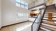 Located at 1571 North Pine Cliff Drive in Flagstaff, Arizona, this contemporary two-story home offers three bedrooms and three bathrooms across two thoughtfully designed floors. The main level immediately impresses with its dramatic double-height ceilings and an abundance of natural light pouring in through large windows. The open-concept living area flows seamlessly into the kitchen, which features rich warm-toned cabinetry, granite-style countertops, a generous peninsula with a built-in sink, stainless steel appliances including a refrigerator, range, and microwave, and stylish pendant lighting accented by exposed wood beams overhead. Light wood-look flooring runs throughout both floors, complementing the clean white walls and dark baseboards. A sleek modern staircase with a black metal railing leads to the upper level, where the bedrooms are situated. The primary bedroom is well-proportioned, featuring soaring ceilings, a ceiling fan, and multiple windows that fill the room with natural light. Additional bedrooms offer closet storage and easy access to the hallways. The three bathrooms are finished with wood-tone vanities, granite-style countertops, and wood-look flooring — two featuring tub-shower combos and one with a walk-in shower with grab bar. The upper landing, framed by a modern metal railing, provides an open and airy transition between levels.