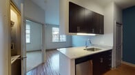 This single-floor residence at 1055 Stratford Ave in Stratford, Connecticut offers a clean, contemporary design with a cohesive open-concept layout. The kitchen serves as a functional centerpiece, featuring dark espresso cabinetry with brushed chrome hardware, granite-look countertops, a stainless steel sink, and stainless steel appliances including a range, microwave, and dishwasher. A peninsula counter connects the kitchen to the living area, creating a seamless flow between the two spaces.

The living area is finished with warm hardwood-style flooring and receives natural light through a generously sized window that frames views of the surrounding residential community. Neutral gray walls provide a versatile backdrop throughout the main living spaces. A separate room, carpeted for comfort, also benefits from a large window with exterior views, offering a quiet and bright retreat.

The hallway connects the main living areas to the bathroom, which is finished with light tile flooring, a dark vanity with a white countertop, and a full tub and shower combination with tiled surround. The overall design of the unit is modern and understated, with consistent finishes and a practical flow from room to room.