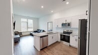 This well-appointed 2-bedroom, 2-bathroom unit offers a thoughtfully designed, single-floor layout with a clean, contemporary aesthetic. The open-concept kitchen and living area forms the heart of the space, anchored by a large granite-topped island with an undermount sink that doubles as a breakfast bar. The kitchen is outfitted with crisp white shaker-style cabinetry with matte black hardware, a light subway tile backsplash, and a full suite of stainless steel appliances including a refrigerator, range, over-the-range microwave, and dishwasher. Warm hardwood-style flooring runs throughout the entire unit, complementing the bright white walls and recessed lighting. The living area receives natural light through large windows fitted with horizontal blinds. Both bedrooms are comfortably sized, with the primary bedroom offering a ceiling fan, natural light from a window, and direct access to a bathroom. The second bedroom also features a window and ample floor space. Each bathroom is finished with white cabinetry, granite countertops, undermount sinks, and large mirrors. The overall ambiance is modern, clean, and functional, making efficient use of the available floor space.