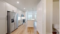 Located at 930 Ridgeview Dr in Allen, TX, this thoughtfully designed two-story home offers a bright, modern living experience across two well-appointed floors. The main level showcases a standout kitchen featuring floor-to-ceiling gray shaker cabinetry, stainless steel appliances including a French door refrigerator, electric range, and built-in microwave, complemented by a large central island with a granite countertop, undermount sink, and elegant pendant lighting. Light wood-look flooring runs throughout, enhancing the clean, contemporary aesthetic. The living area benefits from soaring double-height ceilings with expansive windows that flood the space with natural light, and a modern ceiling fan adds comfort. A dedicated laundry area is equipped with a full-size Whirlpool front-loading washer and dryer. The two bathrooms are finished with granite-topped shaker vanities and wood-look flooring; one features a tiled tub-shower combination, while the other offers a sleek half-bath configuration. A closet provides additional storage. The upper level, accessed via a modern staircase with black metal railing, overlooks the dramatic main living area, completing this efficient yet stylish multi-level home.