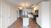This 1-bedroom, 1-bathroom unit offers a thoughtfully designed single-level layout that maximizes functionality and comfort. The open-concept living and kitchen area serves as the heart of the home, featuring warm hardwood-style flooring throughout, neutral-toned walls, and recessed lighting that creates a bright and welcoming ambiance. A pendant-lit drum ceiling fixture adds a refined touch to the living space, which is bathed in natural light from a large floor-to-ceiling window.

The kitchen is well-equipped with a full suite of stainless steel appliances, including a gas range, built-in microwave, dishwasher, and a French door refrigerator. White shaker-style cabinetry pairs cleanly with dark quartz countertops and a subtle tile backsplash. A central kitchen island provides additional prep space and casual seating. Track lighting overhead ensures excellent task illumination throughout the kitchen.

The bedroom offers a comfortable retreat with plush wall-to-wall carpeting, a ceiling fan, and a large window that frames exterior views and fills the room with natural light.

The bathroom is finished in a clean, modern style with a full soaking tub and shower combination, white subway tile surround, chrome fixtures, and a white vanity with ample storage. The overall design of this unit reflects a contemporary aesthetic with practical, high-quality finishes throughout.