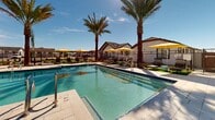 Located in Sun City, Arizona, this single-level outdoor amenity area offers a resort-inspired pool experience designed for relaxation and leisure. The centerpiece is a generously sized, crystal-clear swimming pool with blue tile accents and multiple stainless steel entry rails for easy access. The surrounding pool deck is finished in light-colored pavers that reflect the bright Arizona sun, creating a clean and inviting atmosphere.

Tall, mature palm trees are thoughtfully positioned throughout the space, providing natural shade and a distinct desert-resort aesthetic. The deck is well-appointed with cushioned chaise lounges and dark-framed chairs arranged in clusters, accompanied by vibrant yellow market umbrellas that add a pop of color against the vivid blue sky.

Lush accent landscaping lines the perimeter, softening the hardscape and enhancing the outdoor ambiance. The space is enclosed by a sleek black metal fence, ensuring both privacy and security while maintaining open sightlines to the surrounding community architecture, which features Southwest-inspired rooflines and stucco exteriors.

The overall environment is bright, spacious, and thoughtfully designed to maximize enjoyment of the warm Arizona climate, making it an ideal communal outdoor retreat for residents of this Sun City community.