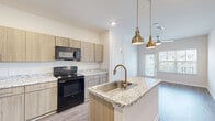 Located at 101 Pine Forest Rd in Augusta, Georgia, this single-floor residence offers a well-designed open-concept layout with contemporary finishes throughout. The kitchen serves as a central highlight, featuring light wood cabinetry, granite-look countertops, and a large center island with an integrated sink and stylish pendant lighting. Black appliances, including a refrigerator, electric range, and over-the-range microwave, complement the modern aesthetic, while durable wood-style flooring ties the space together seamlessly. The kitchen opens toward a bright living area with access to an outdoor space, allowing natural light to flow freely through the unit. The bedrooms are generously sized, carpeted for comfort, and equipped with ceiling fans. At least one bedroom includes a walk-in closet, and an en-suite bathroom features granite-topped cabinetry, a large mirror, and a tub-shower combination. A second full bathroom is also present, finished with the same wood-tone cabinetry and a tub-shower combo. An additional versatile room with wood-style flooring and a large window offers views of the surrounding community. The overall ambiance is clean, bright, and move-in ready, with a cohesive neutral palette throughout.