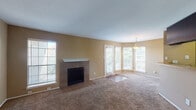 Located at 1109 Meadow Creek Dr in Irving, Texas, this single-story home presents a well-appointed layout with consistent warm-toned walls and plush carpet flooring throughout the main living areas and bedrooms. The spacious living room serves as a central gathering space, highlighted by a tile-surround fireplace with a clean white mantel, multiple windows including a bay window configuration, and a pendant light fixture. Natural light flows generously through the numerous windows, offering pleasant views of surrounding greenery. An adjacent dining or secondary living area connects seamlessly to the kitchen, which features dark espresso cabinetry, gleaming granite countertops, and black appliances including a range, microwave, and dishwasher. The bedrooms are comfortably sized, each equipped with ceiling fans and ample natural light from large windows with outdoor views. Closet space is present in the bedroom areas. The bathrooms are finished with dark cabinetry, granite-style countertops, large mirrors, wood-look flooring, and a tiled tub-shower surround. The overall ambiance is warm and functional, with cohesive finishes carried throughout the home.