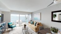 Located at 7901 Harmarsh St in San Diego, this two-floor model home showcases a thoughtfully designed, coastal-inspired interior spread across a well-organized layout. The living room serves as the heart of the home, featuring light wood-style flooring, soft neutral walls, and large sliding glass doors that open to a private outdoor patio — flooding the space with natural light and providing a seamless indoor-outdoor connection. The kitchen is outfitted with white shaker cabinetry, dark countertops, and a full suite of stainless steel appliances including a gas range, microwave, and dishwasher. Adjacent to the kitchen, the dining area comfortably accommodates a four-seat table beneath a modern ceiling fan. The two bedrooms are carpeted and serene, each featuring mirrored sliding closet doors that enhance the sense of space. One bedroom offers expansive windows with treetop views, while the other carries a calming coastal aesthetic with soft blue accents. The bathroom includes a full tub-shower combination with clean white tile finishes and brushed nickel fixtures. Throughout the home, the color palette remains light and airy, creating a cohesive, welcoming atmosphere that reflects the relaxed lifestyle of San Diego living.