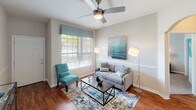 This single-floor residence is thoughtfully designed with a cohesive, coastal-inspired color palette that carries through each room. The living room serves as a welcoming central space, featuring hardwood flooring, a ceiling fan, and a large window that invites natural light and outdoor views. Neutral walls are complemented by teal and gray accents, creating a calm and inviting atmosphere.

The kitchen is efficiently laid out in a galley style, equipped with white cabinetry, light stone-finish countertops, tile flooring, and stainless steel appliances including a refrigerator, range, and microwave. It opens directly to the dining area, which features tile flooring, wainscoting, a statement pendant light, and seating for several guests.

Multiple bedrooms are carpeted and include ceiling fans, natural light from windows with blinds, and neutral walls. Each bedroom offers a comfortable and restful environment, with varying design details ranging from dark wood furnishings to clean white pieces.

The bathrooms feature wood-look flooring, light vanities with stone-finish countertops, and tub-shower combinations with tile surrounds. A hallway thermostat and utility access indicate practical, well-organized infrastructure throughout the home.
