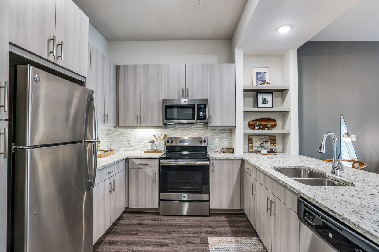 Gray finish package kitchen with speckled granite countertop, stainless steel appliances, and hard surface flooring. - Avalon West Plano