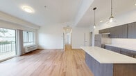 This well-designed 4-bedroom, 2-bathroom home in Lacey, WA offers a thoughtful single-floor layout with a clean, contemporary aesthetic throughout. The open-concept kitchen and living area forms the heart of the home, showcasing dark-toned cabinetry with modern hardware, a white tile backsplash, stainless steel appliances, and a central island with pendant lighting overhead — ideal for both cooking and entertaining. Warm hardwood-style flooring flows seamlessly throughout every room, complementing the crisp white walls and creating a bright, cohesive feel. The living area is generously proportioned, with a sliding glass door opening onto a private balcony with tranquil wooded views. A central hallway connects the four bedrooms, each offering comfortable proportions, large windows that bring in natural light and tree-lined outlooks, and individual wall-unit climate control. Three closets provide ample storage, including walk-in style options with built-in shelving and hanging rods. The two bathrooms are cleanly finished, featuring a walk-in shower with a built-in bench and chrome fixtures. The overall ambiance is modern, light-filled, and move-in ready, with natural surroundings adding a serene backdrop.