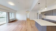 This well-designed 4-bedroom, 2-bathroom home in Lacey, WA offers a thoughtful single-floor layout with a clean, contemporary aesthetic throughout. The open-concept kitchen and living area forms the heart of the home, showcasing dark-toned cabinetry with modern hardware, a white tile backsplash, stainless steel appliances, and a central island with pendant lighting overhead — ideal for both cooking and entertaining. Warm hardwood-style flooring flows seamlessly throughout every room, complementing the crisp white walls and creating a bright, cohesive feel. The living area is generously proportioned, with a sliding glass door opening onto a private balcony with tranquil wooded views. A central hallway connects the four bedrooms, each offering comfortable proportions, large windows that bring in natural light and tree-lined outlooks, and individual wall-unit climate control. Three closets provide ample storage, including walk-in style options with built-in shelving and hanging rods. The two bathrooms are cleanly finished, featuring a walk-in shower with a built-in bench and chrome fixtures. The overall ambiance is modern, light-filled, and move-in ready, with natural surroundings adding a serene backdrop.