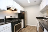 This single-floor residential unit offers a well-organized layout that balances functionality with comfort. The galley-style kitchen is efficiently designed with white shaker cabinetry, dark countertops, wood-look luxury vinyl flooring, and a full suite of appliances including a gas range, refrigerator, and dishwasher. Ample upper and lower cabinet storage lines both sides of the kitchen, maximizing workspace.

The open living area features neutral-toned carpet and connects seamlessly to a dining space illuminated by a pendant chandelier. A door leads out to an outdoor balcony or patio, accompanied by large windows that invite natural light and views of surrounding greenery. A sliding glass door in one room further enhances the indoor-outdoor connection.

The bedrooms are generously sized and carpeted, with neutral wall tones and multiple windows providing natural light. At least one bedroom includes a walk-in closet with built-in shelving and hanging rods, offering substantial storage capacity. The bathrooms feature wood-look flooring, white vanity cabinetry, dark countertops, and tub-shower combinations, presenting a clean and cohesive aesthetic throughout. The overall design emphasizes practical living with consistent finishes across all spaces.