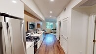 Located at 2727 Mainplace Dr in Santa Ana, CA, this thoughtfully designed 2-bedroom, 1-bathroom residence makes excellent use of its compact footprint. Rich hardwood-style flooring runs throughout the main living areas, tying together a cohesive and contemporary aesthetic. The galley-style kitchen is a standout feature, boasting white lower cabinetry paired with warm wood upper cabinets, a bold black hexagonal tile backsplash, quartz countertops, and a full suite of stainless steel appliances including a gas range, built-in microwave, dishwasher, and French door refrigerator. The open layout allows the kitchen to flow seamlessly into the living room, which is bathed in natural light from large windows offering views of the surrounding greenery. The primary bedroom is a serene retreat with soft carpeting and generous proportions, complemented by a spacious walk-in closet with built-in wire shelving. The second bedroom offers additional flexibility for guests or a home office. The bathroom is clean and modern, featuring large-format white wall tiles, a soaking tub with shower, matte black fixtures, and wood-look flooring that echoes the warmth found throughout the home. Recessed lighting and a crisp white color palette enhance the bright, airy ambiance of the entire residence.