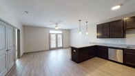 This single-floor residence offers a well-designed open-concept layout that seamlessly connects the kitchen and living area. The kitchen is a standout feature, equipped with rich dark espresso cabinetry extending to the upper walls, light granite countertops, and a full suite of stainless steel appliances including a refrigerator, range, microwave, and dishwasher. An L-shaped peninsula provides additional counter space and casual seating potential. Pendant lighting hangs above the peninsula, adding a modern, polished touch. Light wood-style flooring runs consistently throughout the main living areas, contributing to a clean and cohesive aesthetic. The living area benefits from natural light through a set of double glass doors, complemented by a ceiling fan overhead. The bedroom is generously sized with plush carpeting and a large window that invites natural light. A set of double doors opens to a walk-in closet. The bathroom features matching granite countertops, a dark vanity with an undermount sink, a large framed mirror, and light wood-style flooring that ties the space together. Overall, the unit presents a contemporary and practical living environment with consistent finishes throughout.