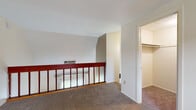 Located at 4391 Woodglen St in Kent, Ohio, this two-story home offers a straightforward layout spread across two levels connected by a carpeted staircase with warm wood railings and balusters. The main level features a living area with plush carpet flooring that transitions into a tiled dining and kitchen space. The kitchen is equipped with wood cabinetry and overhead lighting, offering a functional setup. A sliding glass door on the main level allows natural light to fill the room while providing direct access to the outdoors, with views of surrounding greenery visible through vertical blinds. Vaulted ceilings on the main level contribute to an open, airy feel, enhanced further by skylight-style clerestory windows that introduce additional natural light from above. The upper level, also carpeted, features angled ceilings that follow the roofline, creating a cozy atmosphere. An open railing overlooks the staircase landing below, adding visual connectivity between the floors. A walk-in closet provides ample storage, and a bathroom with a shower/tub combination, wall-mounted cabinet, and standard fixtures rounds out the upper level. The home's neutral color palette throughout lends a clean, versatile canvas well-suited for a variety of interior styles.