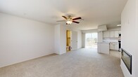 This two-story residence is thoughtfully laid out across two equally proportioned floors, offering a functional and comfortable living environment. The main floor features a welcoming entrance that leads into an open living room with neutral carpet flooring and a ceiling fan with light fixture, creating a bright and airy atmosphere. A sliding glass door connects the living area to an outdoor space, filling the room with natural light. Adjacent to the living area, the kitchen is well-appointed with crisp white shaker-style cabinetry, light marble-look countertops, a classic white subway tile backsplash, and a full suite of stainless steel appliances including a range, over-the-range microwave, refrigerator, and dishwasher. Light wood-look tile flooring completes the kitchen's clean, modern aesthetic. Three bathrooms are distributed throughout the home; each features white cabinetry with brushed nickel hardware, marble-look countertops, and tile flooring, with at least one including a full tub-shower combo with tiled surround. Carpeted stairs with a handrail lead to the upper floor, where the generously sized primary bedroom offers ample space and is accompanied by a dedicated walk-in closet with built-in wire shelving for organized storage. The upper level also features an open loft-like area with elevated windows that allow in natural light. The home's consistent neutral palette and modern finishes create a cohesive and move-in-ready living space.