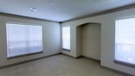 This single-floor space is thoughtfully designed with a clean, neutral aesthetic that creates a calm and inviting environment. The interior is finished with warm beige walls and complementary gray baseboards that frame each room with a polished, cohesive look.

The main living area is carpeted in a plush, light-toned material that adds comfort underfoot and contributes to the overall warmth of the space. A standout architectural feature is the arched alcove built into one wall — a distinctive design element that adds visual interest and character, serving as a decorative niche or functional display area.

Natural light is a key feature throughout, with multiple windows dressed in white horizontal blinds that allow for adjustable light control while maintaining a tidy appearance. The bright, white ceiling is fitted with recessed vents, contributing to a clean overhead finish and efficient climate management.

The overall ambiance is neutral, move-in ready, and versatile — well-suited to a variety of interior styles and furnishing arrangements. The combination of soft carpeting, arched detailing, and ample natural light makes this a comfortable and functional space ideal for everyday living.