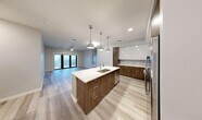 Located at 1721 Motor Parkway in Hauppauge, NY, this well-appointed 3-bedroom, 4-bathroom residence offers a thoughtfully designed single-floor layout with generous living space. The open-concept kitchen and living area serves as the heart of the home, showcasing a large center island with a sleek quartz countertop, undermount sink, and striking two-tone cabinetry — rich walnut lowers paired with crisp white uppers — complemented by a tile backsplash and stainless steel appliances. Pendant lights above the island add a modern touch. The living area extends toward floor-to-ceiling glass doors that open onto a private balcony, filling the space with natural light. Light-toned hardwood-style flooring flows throughout the main living areas, while the bedrooms are finished with plush carpeting. The generously sized primary bedroom includes a walk-in closet with custom shelving and hanging rods. The bathrooms feature clean, modern fixtures with marble-style tile flooring and frameless mirrors. A dedicated laundry room houses a full-size side-by-side washer and dryer. Three additional closets provide ample storage throughout the residence, rounding out a practical and refined living experience.