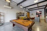 Located at 820-828 Ralph McGill Blvd NE in Atlanta's Old Fourth Ward, this single-floor amenity lounge showcases a bold industrial-chic aesthetic throughout its open layout. Polished concrete floors, exposed steel beams, painted cinder block walls, and black structural piping running across the ceiling establish a raw, warehouse-inspired character that is complemented by carefully curated furnishings and artwork.

The space is organized into distinct activity zones. A full-size pool table anchors one area, accompanied by a dartboard and shuffleboard for recreational use. A large garage-style window wall floods the room with natural light and provides views of the outdoor greenery beyond. Comfortable leather lounge chairs cluster near a bold, large-scale abstract painting, while a vibrant yellow sectional sofa and industrial-style dining table with crank stools offer additional seating.

A built-in bar and kitchenette area features a concrete island with bar stools, open shelving, a beverage refrigerator, and a mounted TV — ideal for social gatherings. Decorative highlights include a striking amber-glazed tile accent wall with a sliding barn door, a repurposed vintage car body fashioned into a lounge chair, and a collection of framed black-and-white photographs. Industrial pendant lighting throughout ties the eclectic, creative atmosphere together cohesively.