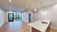 Located at 900 E Market St in Greensboro, North Carolina, this modern single-floor residence offers a thoughtfully designed open-concept layout with clean lines and contemporary finishes throughout. Light hardwood flooring flows seamlessly across the main living areas, complementing the neutral color palette and creating a bright, cohesive aesthetic.

The expansive living area is anchored by striking floor-to-ceiling windows and a glass-panel balcony door that floods the space with natural light and provides views of the surrounding Greensboro cityscape. The kitchen is well-equipped, featuring rich dark wood cabinetry, stainless steel appliances, white quartz countertops, a functional island with an undermount sink, and stylish pendant lighting overhead — ideal for both everyday cooking and entertaining.

The bedroom offers a ceiling fan, large windows with urban views, and access to a walk-in closet with built-in shelving. The bathroom is finished with marble-style tile flooring, a dark wood vanity with white countertop, and a large mirror with modern fixtures. A second full bathroom with tile flooring and a toilet is also accessible from the hallway.

A spacious hallway connects all areas of the unit efficiently, with recessed lighting and panel-style interior doors adding to the polished, modern feel of this well-appointed Greensboro residence.