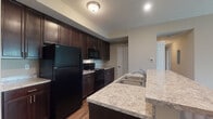 Located at 1 Kerry Park Cir in Delaware, Ohio, this single-floor residence offers a well-designed layout with a cohesive, modern aesthetic throughout. The kitchen is a standout feature, showcasing rich dark-espresso cabinetry, light granite countertops, and a full suite of black appliances including a refrigerator, range, and over-the-range microwave. A peninsula with an overhang provides additional seating and separates the kitchen from the living area, enhancing the open-concept feel. Durable hardwood-style flooring runs through the kitchen and main living areas, adding warmth and easy maintenance. The bedrooms are carpeted for comfort, each featuring neutral tones, natural light from windows with blinds, and generous closet space with built-in shelving and hanging rods. Two bathrooms serve the residence: one features a sleek sliding-glass enclosed shower stall with a vanity topped in matching granite and dark cabinetry, while the second is a more utilitarian full bath with tile flooring and a tub/shower combination. Throughout the home, neutral wall tones, clean white trim, and consistent finishes create a cohesive and move-in-ready environment well-suited for comfortable everyday living.
