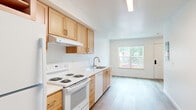 This two-story, two-bedroom, two-bathroom home offers a well-organized layout spread across two evenly sized floors, connected by an interior staircase. The main floor features an open-concept kitchen and living area finished with light hardwood-style flooring and crisp white walls. The kitchen is equipped with warm honey-toned wood cabinetry, white appliances including an electric range, dishwasher, and refrigerator, complemented by clean white countertops. A window in the living area brings in natural light and offers views of surrounding greenery, creating a bright and airy atmosphere. The upper floor houses both bedrooms, a hallway, and the two bathrooms. Each bedroom features light hardwood flooring, ceiling fans, and windows that let in generous natural light with outdoor views. The bedrooms include open closets with hanging rods for practical storage. The bathrooms are finished with warm wood vanity cabinets, white countertops, and full tub-shower combinations. Throughout the home, natural wood-finish doors add a warm, modern touch against the clean white walls and trim. The overall design is clean and contemporary, offering a functional and comfortable living environment.