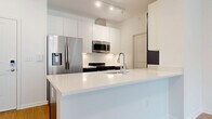 Located at 200 Townsfolk Alley in Penfield, NY, this well-designed two-bedroom, two-bathroom residence offers a thoughtful single-floor layout with a clean, contemporary aesthetic throughout. Entry is through a paneled white door equipped with a smart lock, opening into a bright, neutral-toned interior with warm hardwood-style flooring in the main living areas.

The kitchen is a standout feature, boasting sleek white upper cabinetry, dark lower cabinets with an accent navy wall, stainless steel appliances including a French door refrigerator, built-in microwave, and range, as well as a white quartz countertop with an integrated sink and peninsula for added prep space. Track lighting overhead adds a modern touch.

The open living room benefits from warm hardwood-style flooring and a sliding glass door that leads to an outdoor balcony, filling the space with natural light and views of surrounding greenery. Both bedrooms feature plush carpeting and sizable windows that frame lush outdoor views, creating a serene, comfortable atmosphere. The primary bedroom is generously proportioned with two windows for ample daylight.

The bathrooms are finished with wood-look flooring, contemporary slate-blue vanities with white countertops, and a glass-enclosed walk-in shower. Two closets provide practical storage throughout the unit, completing this well-appointed residence.