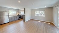 This single-floor residence presents a thoughtfully updated interior with a cohesive neutral palette and modern finishes throughout. The open-concept living and kitchen area serves as the heart of the home, featuring light hardwood-style flooring that enhances the sense of space and continuity. Natural light flows in through multiple windows, offering pleasant outdoor views of surrounding greenery.

The kitchen is a standout feature, showcasing grey shaker-style cabinetry paired with crisp white quartz countertops and a textured tile backsplash that extends to the ceiling. Stainless steel appliances include a gas range with a sleek wall-mounted hood, a dishwasher, and a refrigerator, all complemented by recessed and pendant lighting.

The bedrooms are carpeted in a warm neutral tone, each equipped with recessed lighting and windows that bring in natural light. One bedroom includes a dedicated closet and direct access to a utility area housing a stacked washer and dryer.

The bathrooms are finished with contemporary fixtures, including a full bath featuring large-format wall tiles, a soaking tub with a frameless sliding glass enclosure, and a vanity with a marble-style countertop and polished chrome hardware.