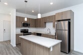 Located at 12191 W Delmar St in Boise, Idaho, this two-story home offers a clean, contemporary design with thoughtful finishes throughout both levels. The main floor features an open-concept layout connecting the kitchen and living areas, with durable wood-look flooring that extends through the hallways and common spaces. The kitchen is well-appointed with flat-front wood-toned cabinetry, white quartz countertops, a central island with pendant lighting, and a full suite of stainless steel appliances including a range, over-the-range microwave, dishwasher, and refrigerator. A convenient half-bath with a pedestal sink is also located on the main level. Natural light flows through large windows toward the front of the home, enhancing the bright, airy atmosphere. The staircase leads to the upper level, where carpeted bedrooms offer comfort and quiet. The primary bedroom features vaulted ceilings and a window with outdoor views, adding a sense of spaciousness. Additional bedrooms are generously sized with ample closet space. Full bathrooms on the upper level are finished with wood-toned vanities, white countertops, and wood-look tile flooring. The overall aesthetic is modern and move-in ready, with consistent, cohesive design choices from top to bottom.