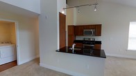 This two-story residence offers a thoughtfully designed layout that combines modern aesthetics with functional living. The open-concept kitchen serves as a central highlight, showcasing deep black granite countertops that extend across a generous breakfast bar, providing both workspace and casual dining. Rich, warm-toned wood cabinetry offers ample storage, while stainless steel appliances — including a gas range, built-in microwave, and dishwasher — complete the contemporary culinary space. A sleek, modern faucet and undermount sink add refined detail to the kitchen.

The space benefits from dramatically high ceilings that create an expansive, airy atmosphere, accentuated by an industrial-style track lighting system that runs overhead, providing adjustable, focused illumination. Neutral-toned flooring flows throughout the living areas, complementing the clean, light-colored walls. The vertical scale of the space is further enhanced by the two-floor layout, lending a sense of grandeur rarely found in typical residences. Overall, the design balances urban sophistication with everyday comfort, making it an ideal space for both entertaining and day-to-day living.